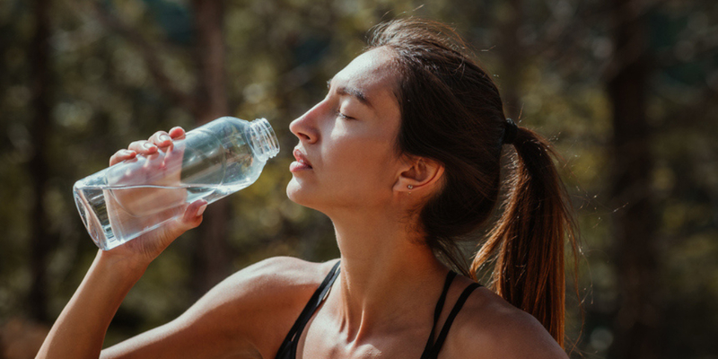 Image of photo of a woman drinking electrolytes from a glass bottle after exercising