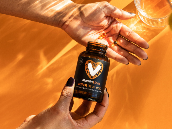 vitamin D supplement with small capsules in a hand on an orange background